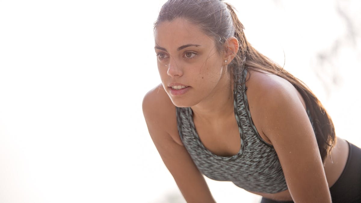 Active woman in workout attire taking a break during exercise outdoors.